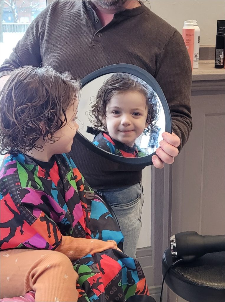 little girl at salon looking in mirror after child's haircut with Norbie